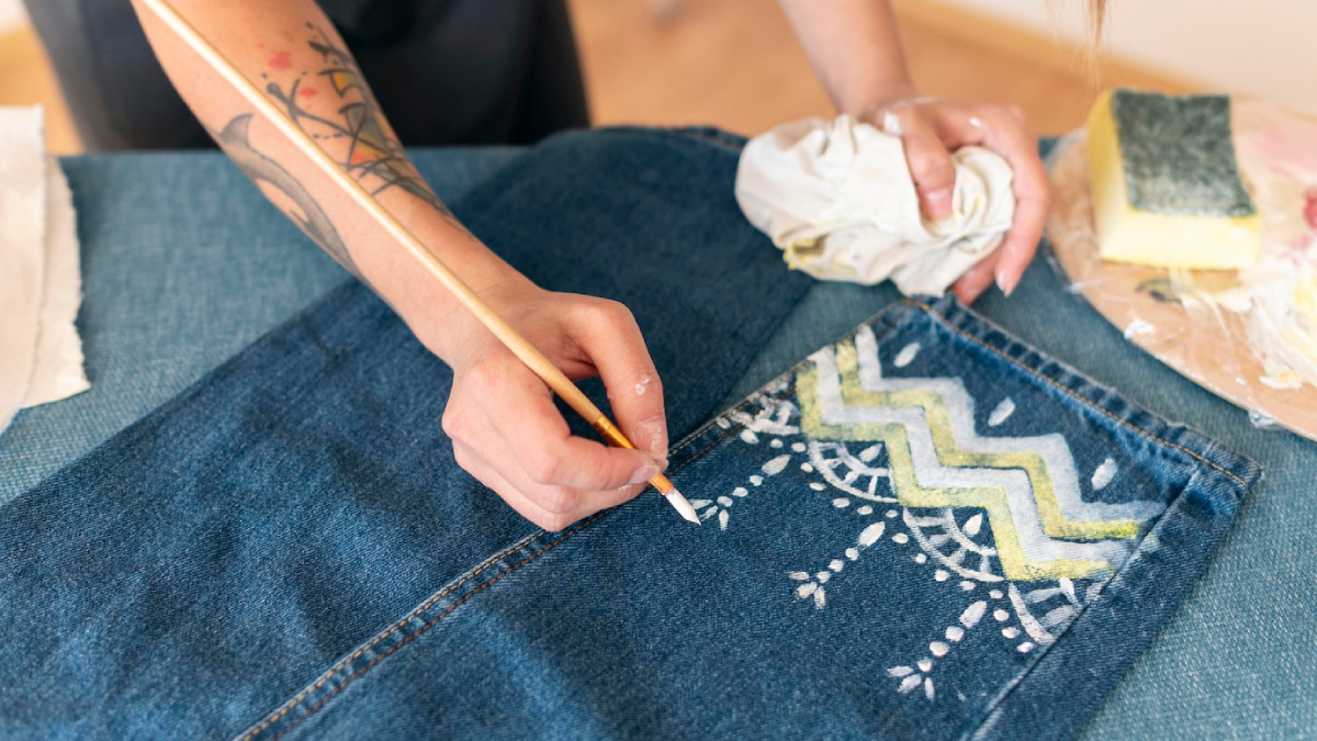 A person paints a decorative pattern on a denim fabric using a brush, showcasing vibrant colors and intricate designs.