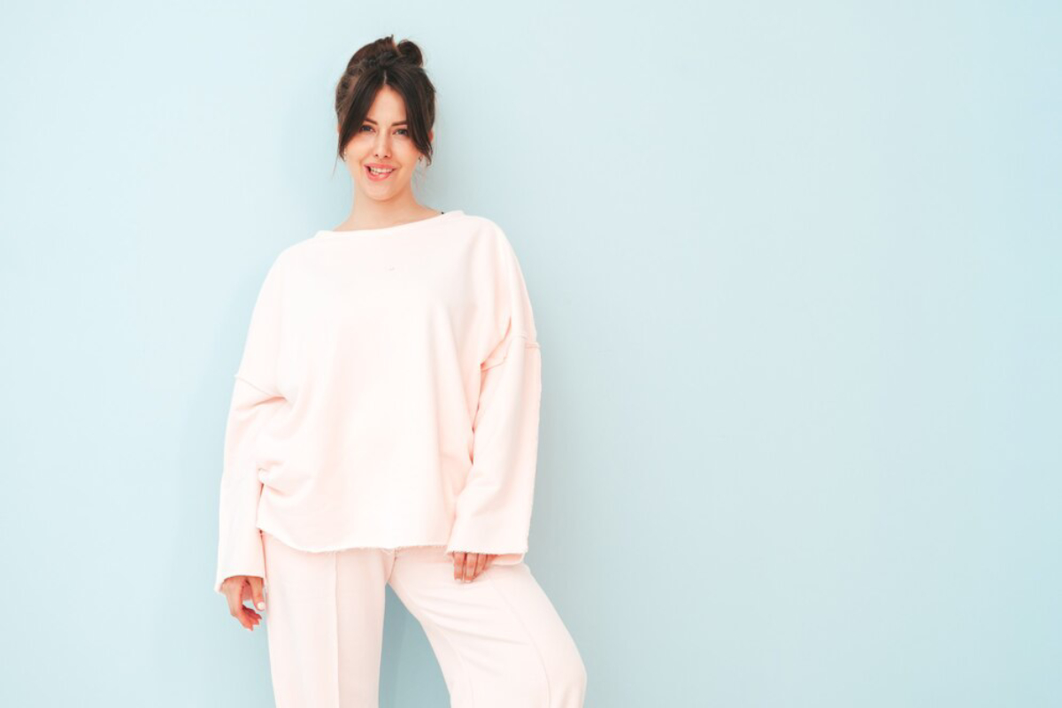 A person in a soft pink oversized sweater and matching pants poses against a light blue background, exuding a relaxed vibe.