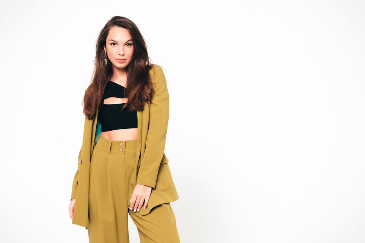 A woman poses confidently in a stylish mustard suit with a black crop top, set against a plain white background.