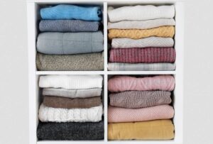 Four drawers containing neatly folded assorted sweaters in various colours and patterns.