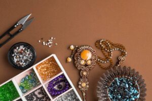 Crafting supplies including beads, scissors, and an ornate pendant on a brown background.