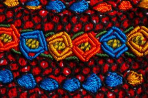 Colourful embroidered fabric featuring detailed, geometric patterns in vibrant red, blue, yellow, and green threads.