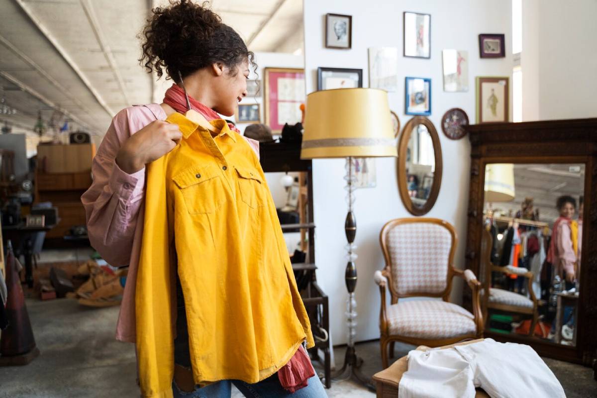 Woman trying on a yellow jacket in a vintage store filled with furniture and mirrors. 