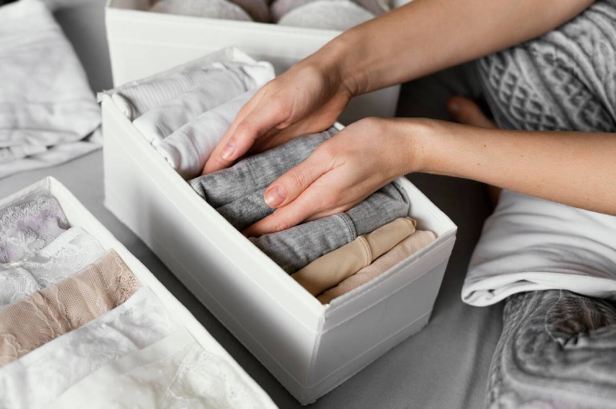 Hands neatly organizing clothes into compartments inside a drawer.