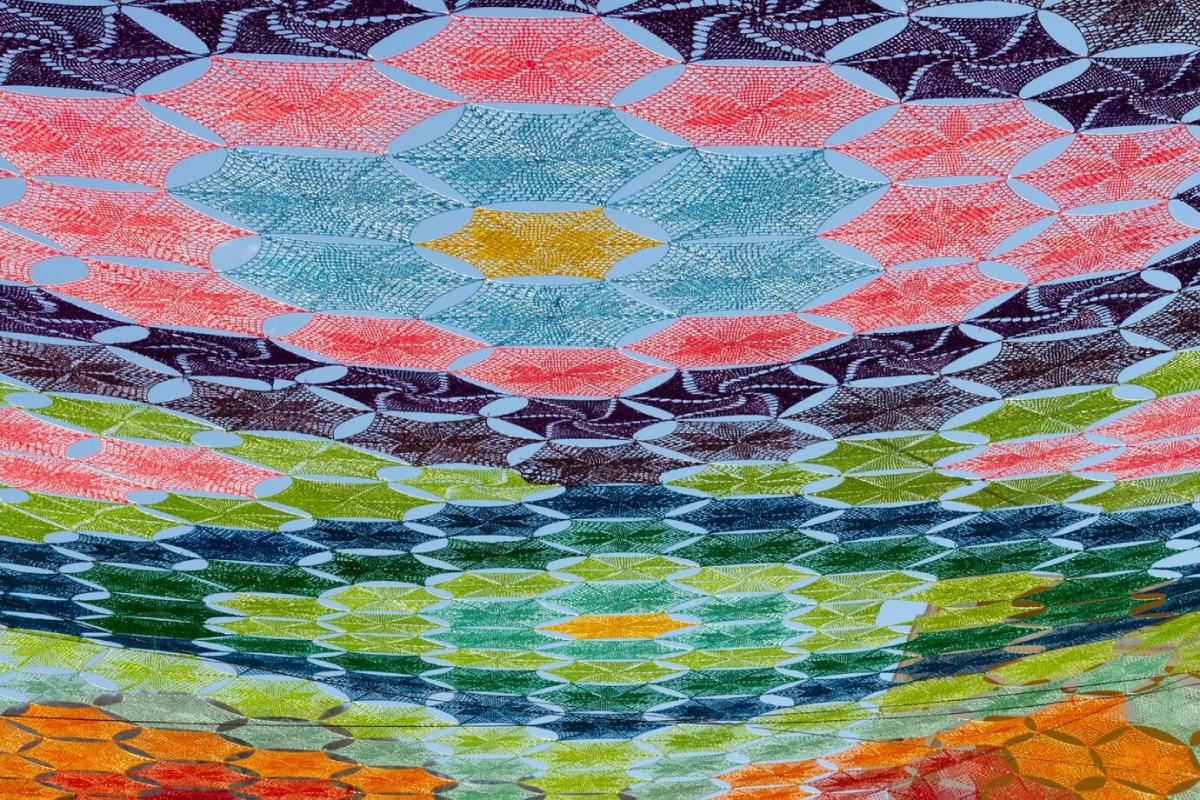 Colourful, abstract textile art featuring an intricate layered pattern of waves in various vibrant hues. 