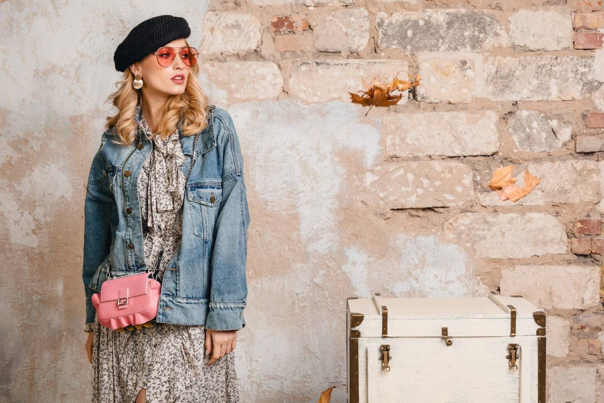  Stylish woman in vintage outfit leaning against a brick wall, next to an old suitcase.