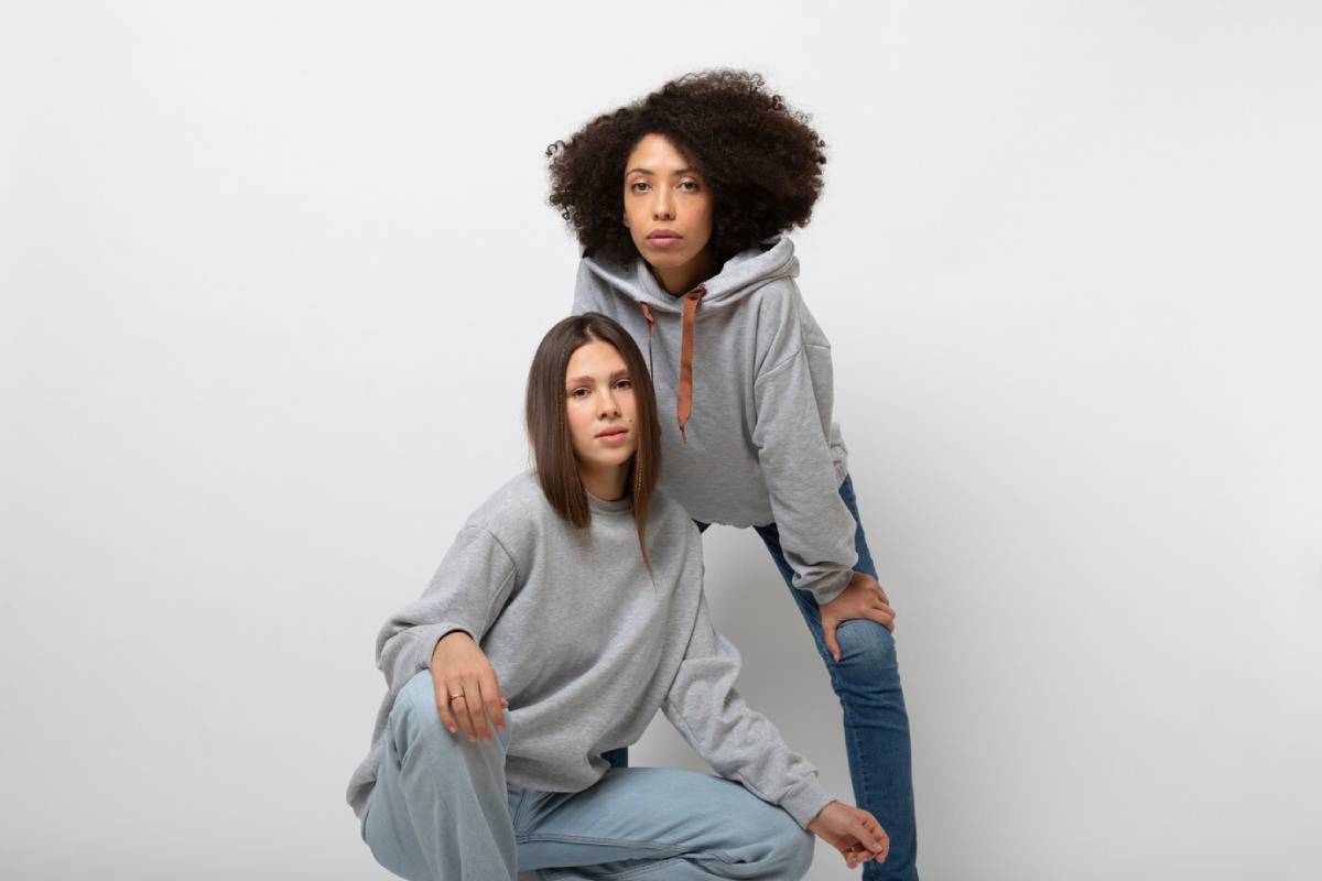  Two young women in casual grey hoodies posing in front of a white background.