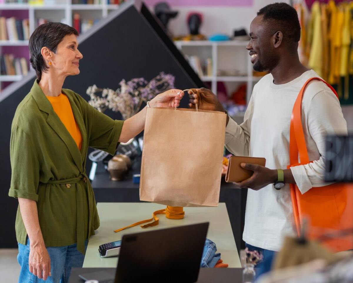 A shopkeeper hands a shopping bag to a happy male customer in a vibrant boutique.