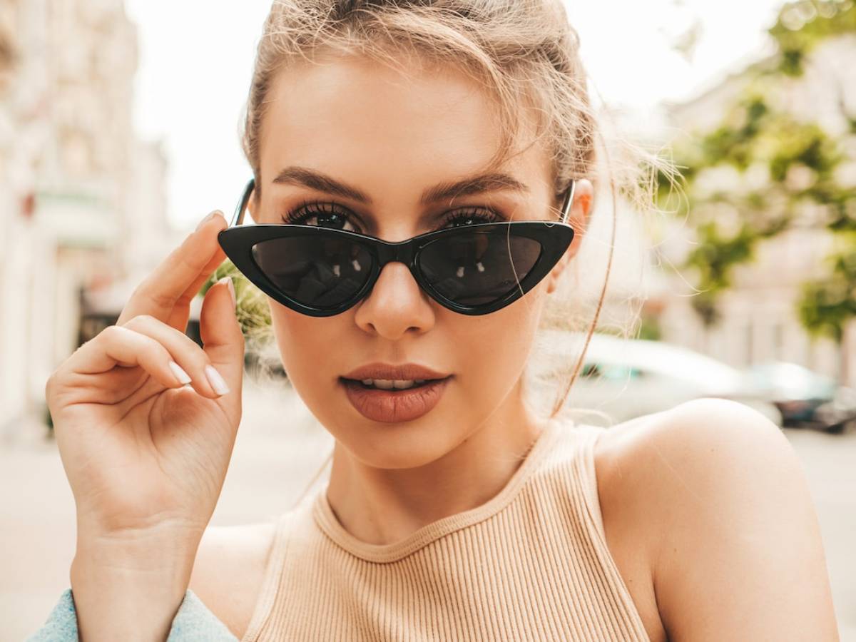 Young woman adjusting her black sunglasses on a sunny city street.