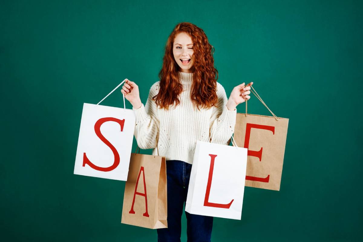 Happy woman holding shopping bags with SALE written on them, against a green background.