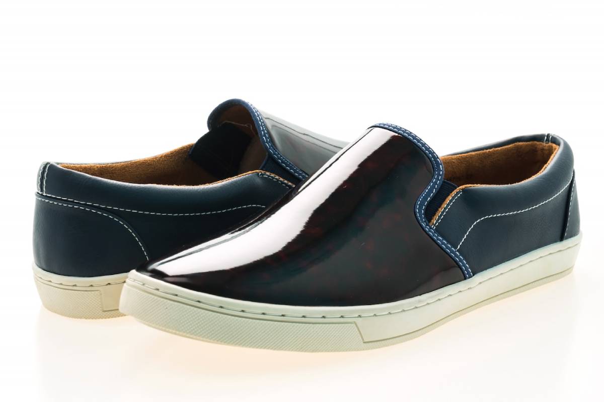 A pair of men's shiny navy blue slip-on shoes with white soles, displayed on a white background.