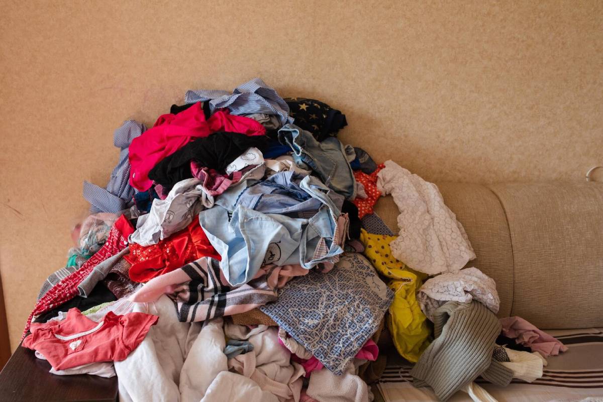  A large pile of various unfolded clothes on a sofa, creating a messy look.