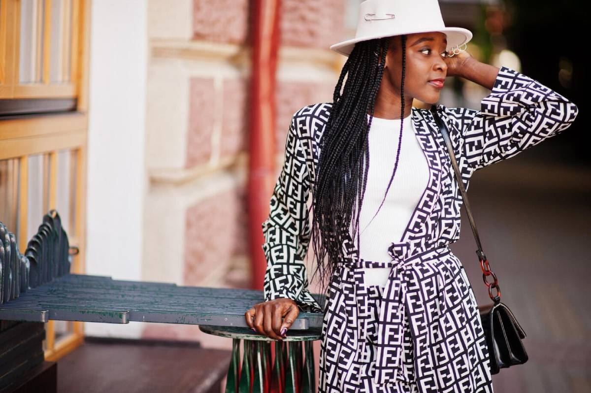  Woman in a stylish geometric print outfit and white hat leaning on a metal bench outdoors.