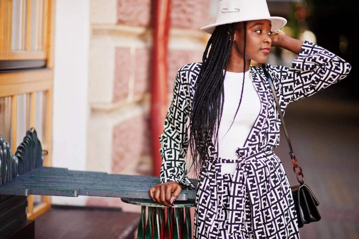 Woman in a stylish geometric print outfit and white hat leaning on a metal bench outdoors.